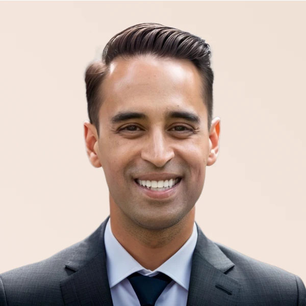 A smiling man in a suit and tie against a light neutral background. His hair is neatly styled, and he is looking directly at the camera.